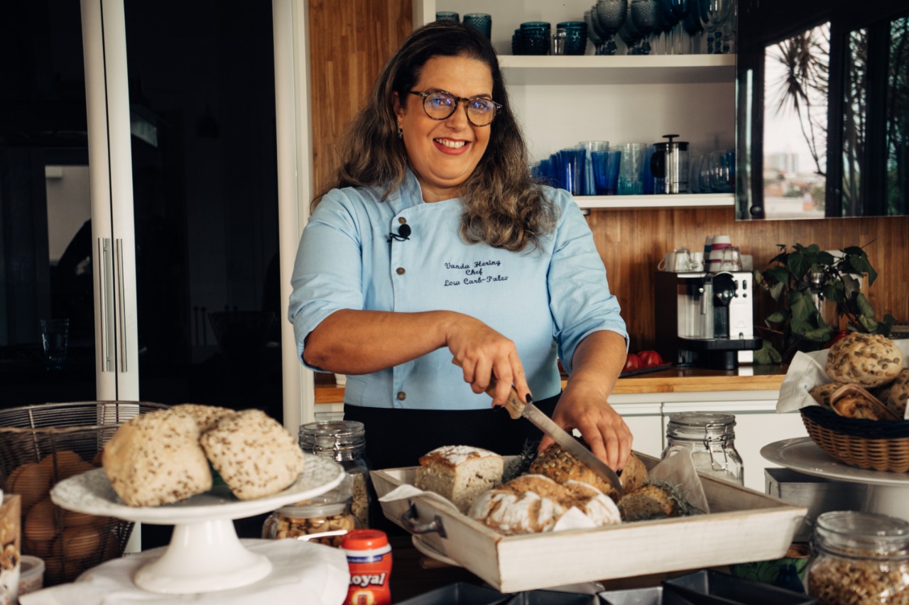 Chef Vanda Hering sorrindo em sua cozinha segurando um pão low carb recém-assado